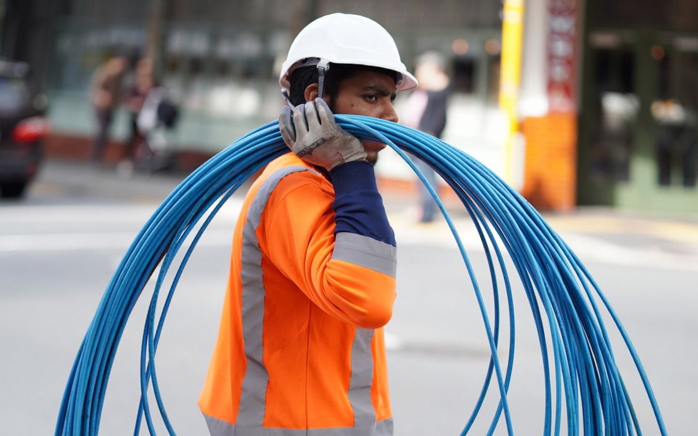 Field worker in high-visibility clothing carrying a coil of blue cable